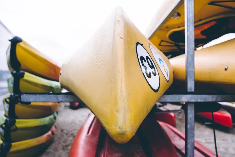 A detailed view of brightly colored kayaks stacked outdoors, focusing on a yellow kayak with numbers