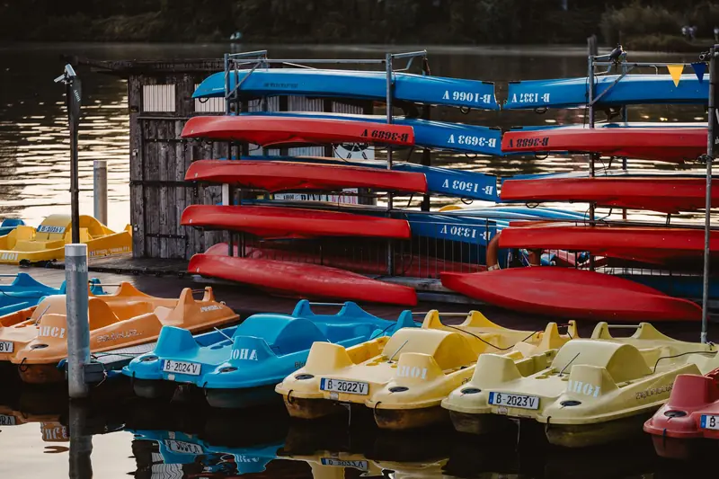 Vibrant pedal boats and kayaks neatly arranged at a lakeside dock, ready for rental