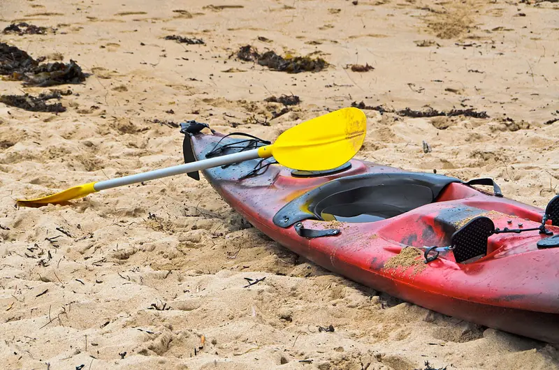 Vibrant red kayak with a yellow paddle on a sandy beach in Gold Coast, Australia