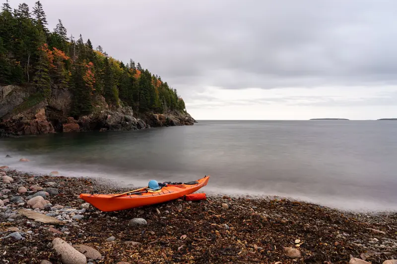 Tranquil autumn shoreline with a kayak, rocky beach, and calming waters