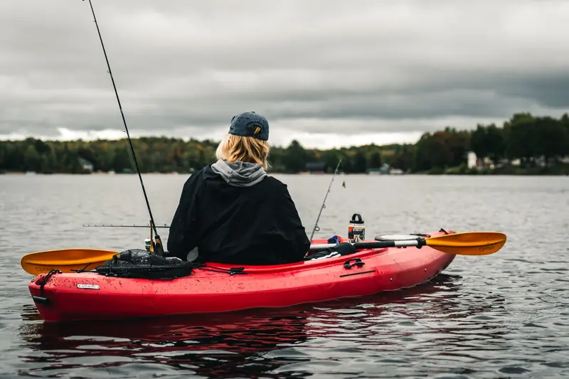 Back view of a person in a red kayak fishing on a tranquil lake with a cloudy sky