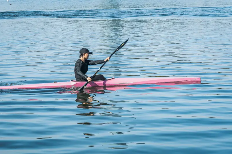 A person kayaking on calm waters in a vibrant pink kayak under clear skies