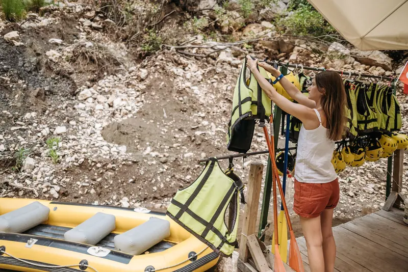 A woman arranges life jackets by a kayak, preparing for a summer adventure outdoors