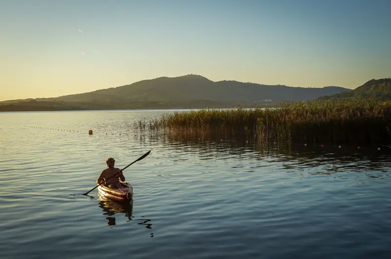 A person kayaks peacefully on a lake during sunset with mountain views
