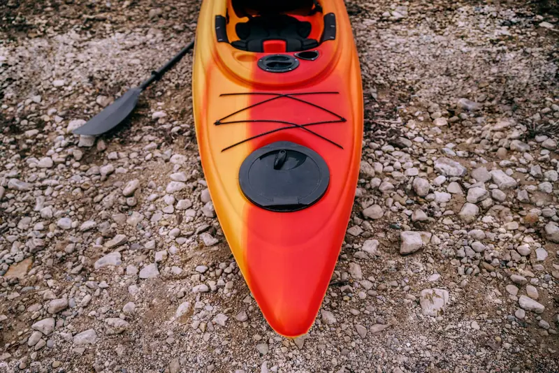 A vibrant red kayak rests on a rocky shoreline, ideal for outdoor adventures