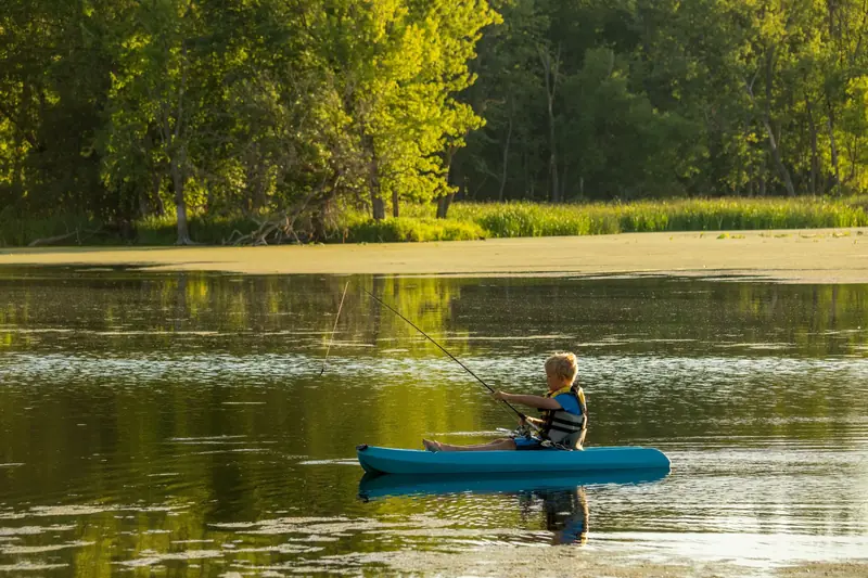 A young boy paddles a kayak while fishing on a serene Minnesota lake, enjoying nature