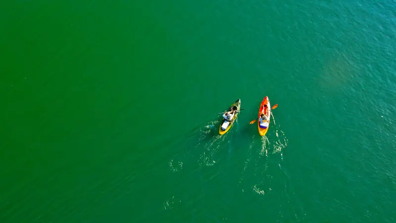 Two colorful kayaks paddle across a vibrant lake in Paulicéia, Brazil, captured from above