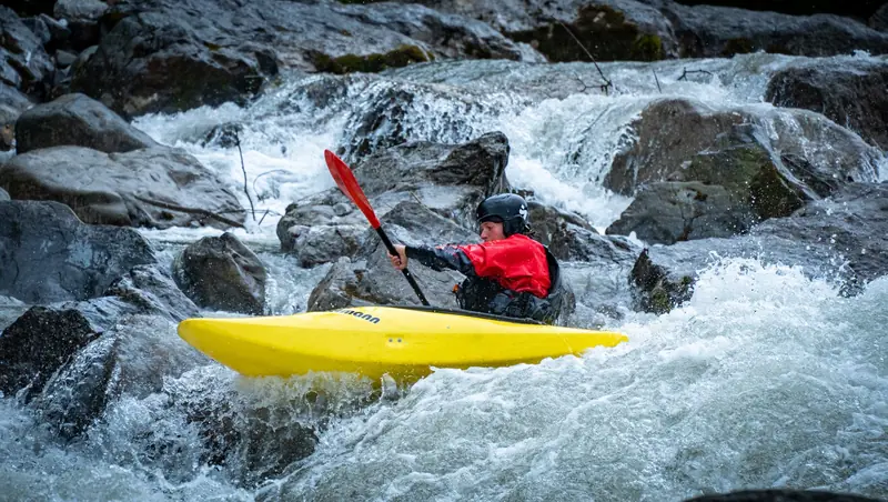 A kayaker skillfully maneuvers through rocky rapids in a vibrant yellow kayak