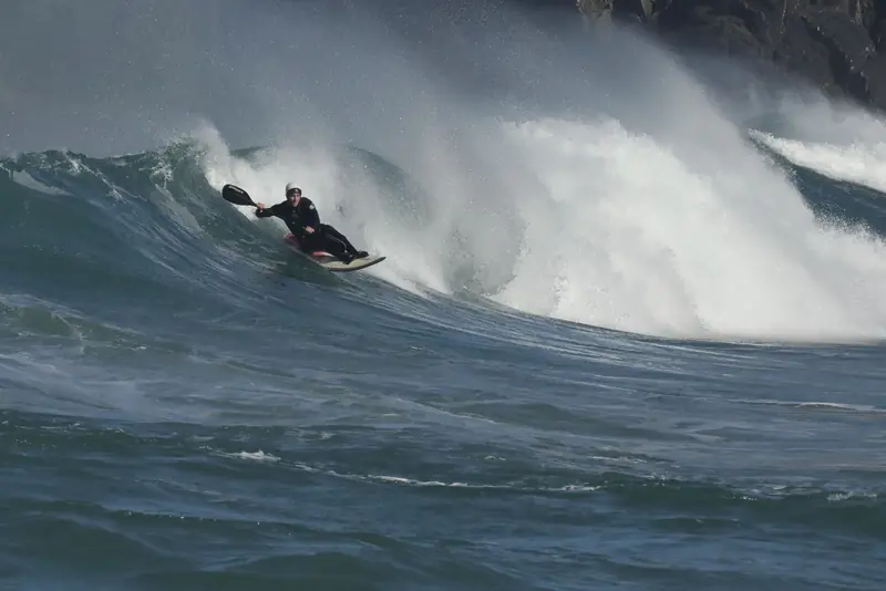 Kayaker tackling large ocean waves, showcasing thrilling water sport adventure