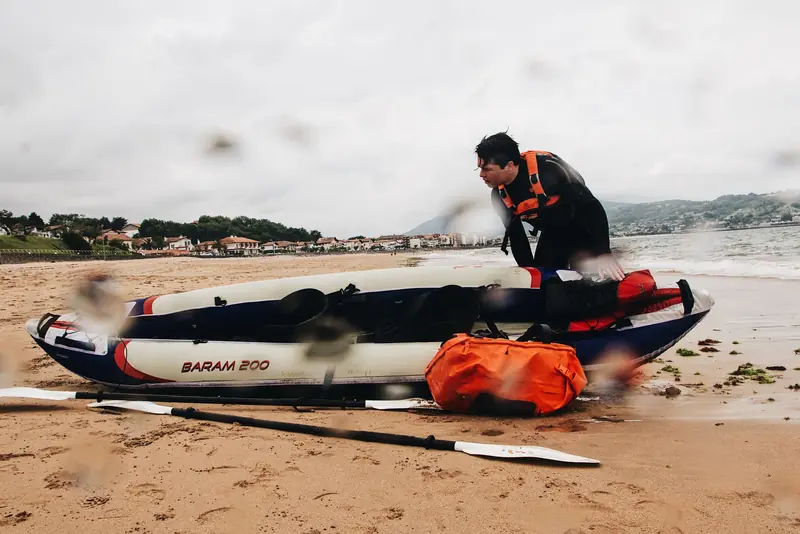 A man in a wetsuit preparing a kayak on a sandy shore, readying for a watersport adventure