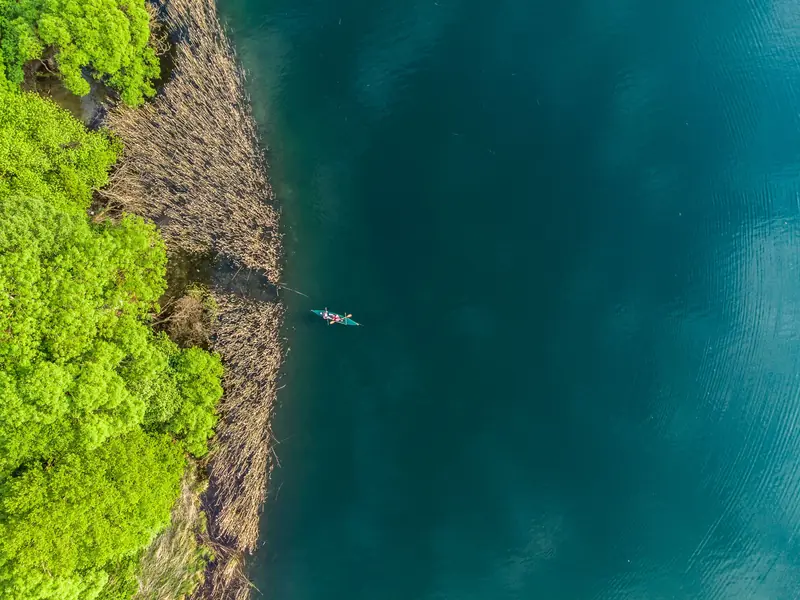 Aerial shot of a kayak gliding through a tranquil lake, bordered by lush greenery