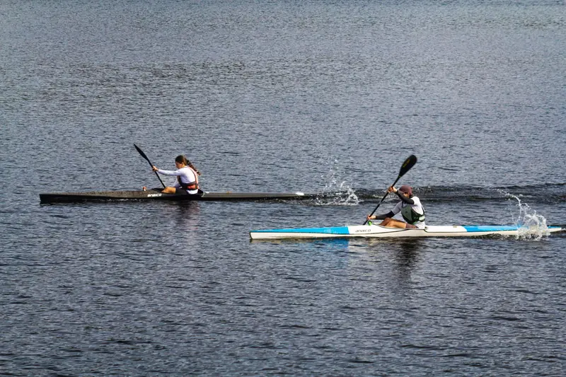 Two athletes paddle fiercely in a kayak race on a calm lake, showing competitive spirit and agility