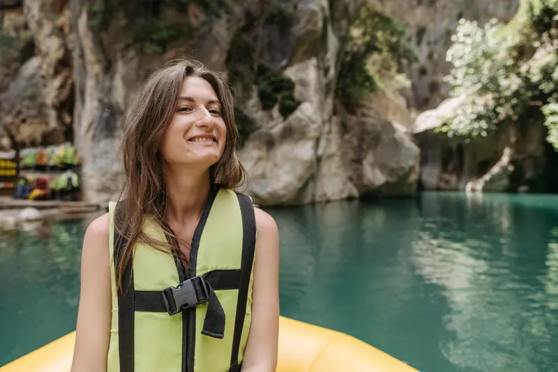 Young woman in a green life jacket smiling on a kayak by a scenic mountain lake