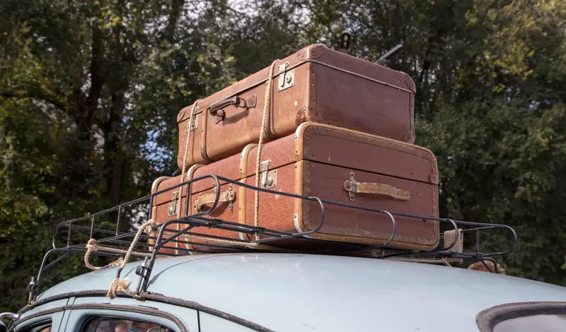 Stack of vintage suitcases secured on a classic car roof rack for an outdoor road trip