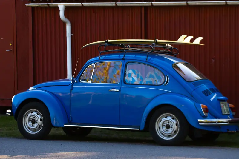 Classic blue VW Beetle car parked outdoors with surfboards on roof rack
