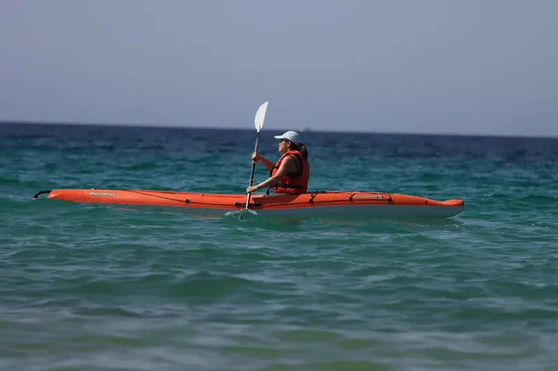 Woman kayaking in vibrant orange kayak on open ocean on a sunny summer day