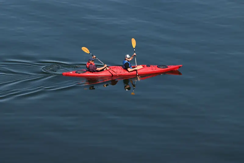 Two people kayaking in a red kayak on a serene lake in Sweden. Outdoor recreation and adventure