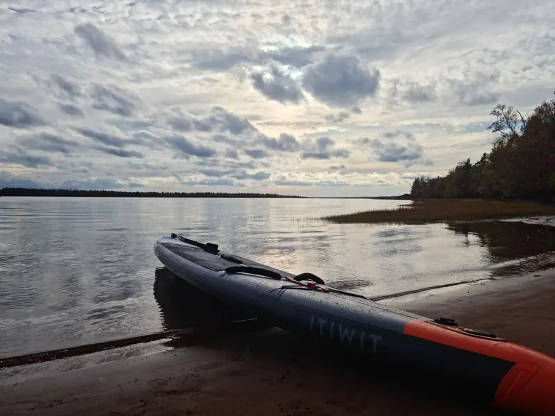 Calm lakeside scene with an inflatable kayak resting on a sandy beach under a cloudy sky