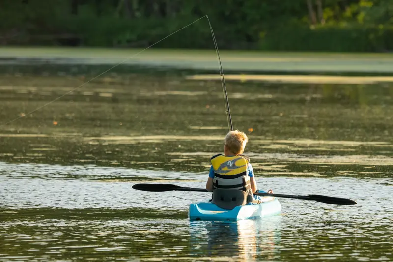 A young boy in a kayak fishing on a serene lake in Minnesota, enjoying an outdoor adventure