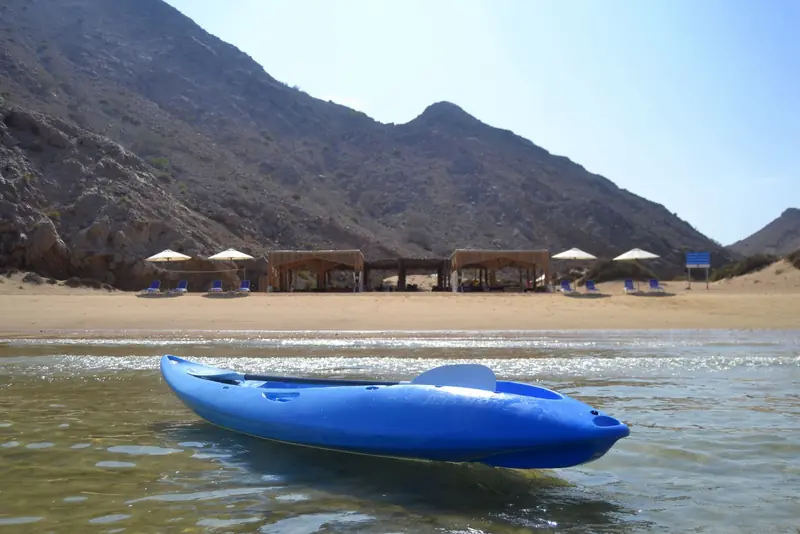 Relaxing scene of a private beach with a blue kayak under sunny skies in Oman